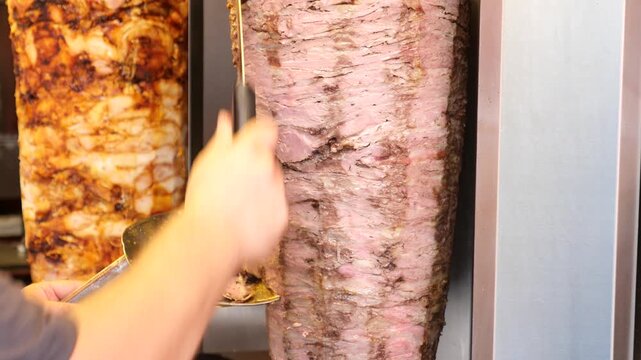 Professional chef cutting thin slices of roasted meat from vertical rotating shawarma spit in street food restaurant