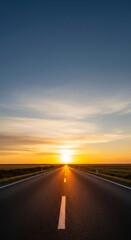 Fototapeta premium Endless asphalt road stretching towards a bright sunset over a grassy field