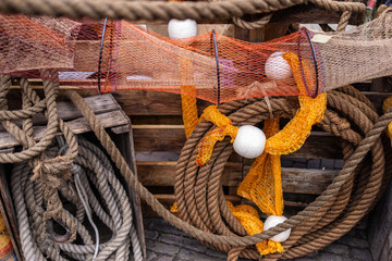 An intricate arrangement of traditional fishing equipment, including thick hemp ropes, bright orange netting, and white floats against a backdrop of weathered wooden crates. © zlatoust198323