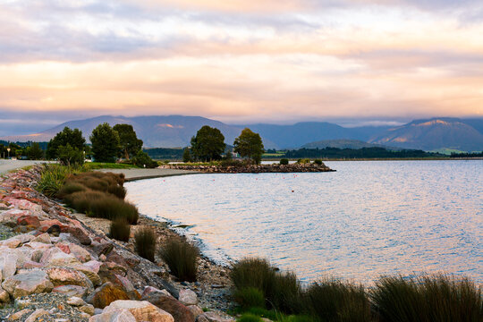 View of a rocky shore line curving out into the lake with sunset colours in clouds and reflections