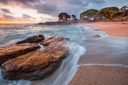Receding waves flowing around shoreline boulders on a rocky coastline in golden dawn light