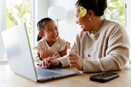 Happy young girl looking at mum while working on her laptop