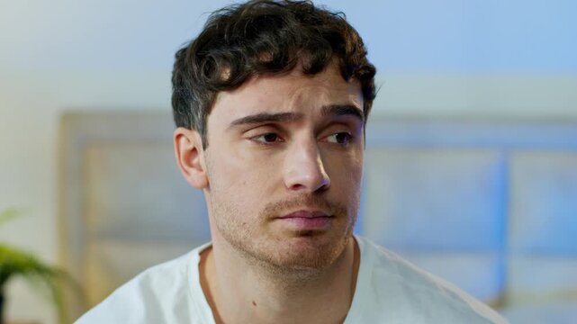 Pensive serious Caucasian man frowning sigh looking at camera thoughtful upset male guy in bedroom contemplating uncertain sadness tired disappointed frustration emotion fatigue face expression indoor