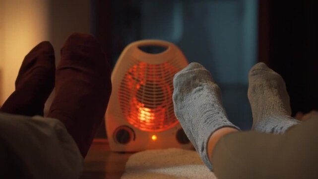 A cozy young couple snuggles on the floor beside a warm heater, clad in winter socks, savoring a cold evenings relaxation at home, fostering togetherness and warmth in their intimate interior space