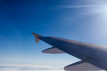 Obraz premium A peaceful and scenic view taken from an airplane window, showing a gray wing extending over a vast, white sea of fluffy clouds under a clear blue sky. This high-altitude perspective captures the sere