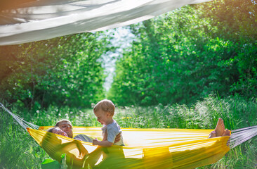 Family relaxing in yellow hammock in sunny green nature