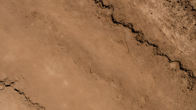 Dry cracked clay soil texture with earthy brown ground and rugged fissure, arid landscape detail conveying warmth and roughness