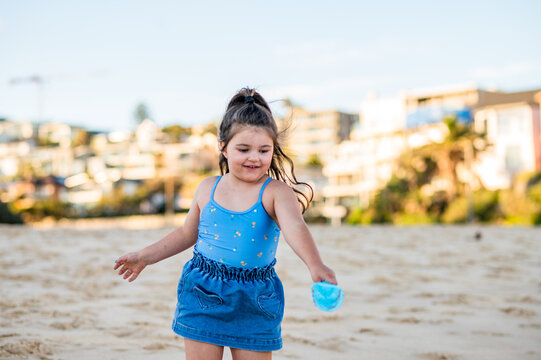 Girl in blue outfit throws sand with spade on beach during afternoon with clear sky