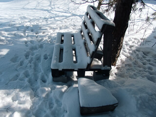 Wooden garden bench made of pallets covered in deep snow under a tree in winter park, black and white photography