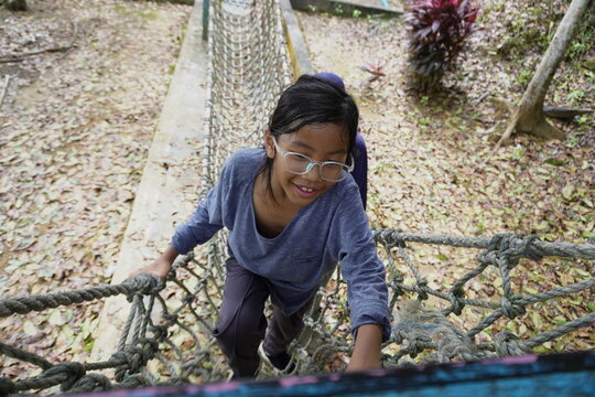  Asian little girl playing on outdoor playground with mother, crossing rope net and swinging on sunny morning, active kids physical activity in nature park