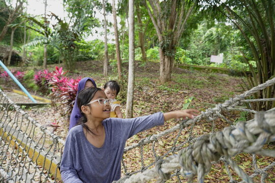  Asian little girl playing on outdoor playground with mother, crossing rope net and swinging on sunny morning, active kids physical activity in nature park