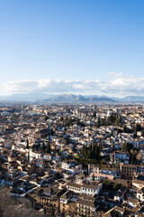 Fototapeta premium A breathtaking panoramic view of Granada stretching below the majestic Alhambra complex, with snow-capped Sierra Nevada mountains in the distance, showcasing Spain's winter tourism appeal.