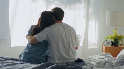 Back view Caucasian man woman couple sitting on bed hugging in bedroom at home boyfriend hug girlfriend together cozy hotel tenant cuddle bond loving tenderness sweetheart harmony wife husband feeling