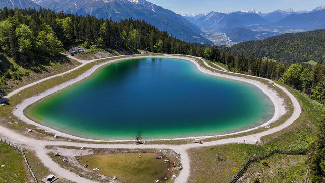 Aerial, bird view, aerial on the storage pond lake on the Gschwandtkopf mountain in Seefeld, tirol, Austria. Beautiful hiking destination. In far background seefeld village and surrounding mountains. 