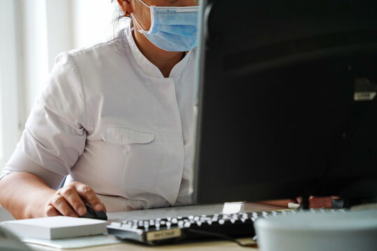 The doctor is sitting at the computer at his desk in the hospital.