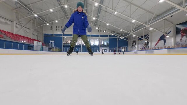 Low angle shot of father and son ice skating over camera, family winter sports activity at indoor rink