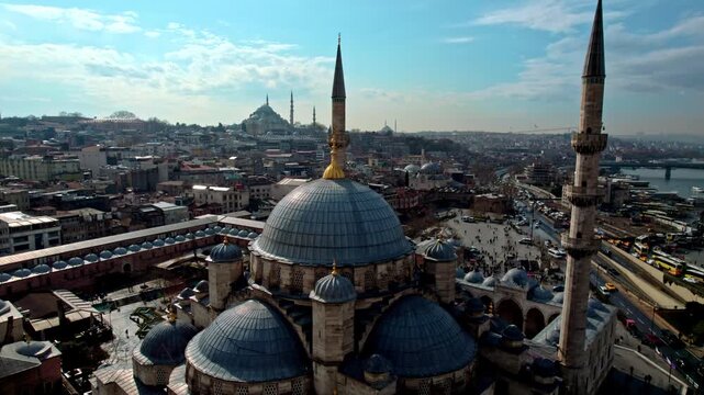 The New Mosque (Emin&ouml;n&uuml;) in the foreground with waterfront roads and traffic. The Galata Bridge spans the Bosphorus, where ferries, boats, and dense urban fabric define the Istanbul cityscape.