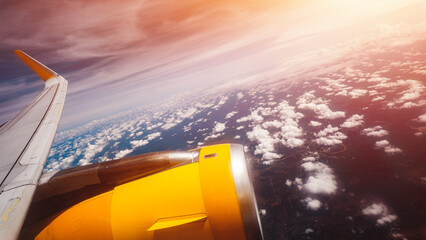 Airplane wing and jet engine above clouds during flight with warm sunset sky, Aerial aviation travel view showing aircraft turbine and wing over cloudscape and earth horizon