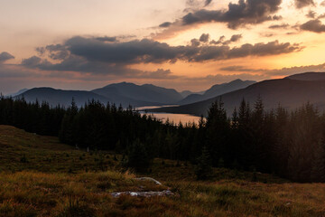 Obraz premium Sunset silhouette of forest and mountains over Loch
