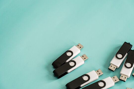 Multiple black and white USB flash drives placed in a minimal composition on a turquoise surface, representing portable data storage and digital technology.
