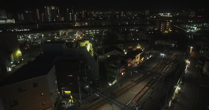 Slow train moving under patches of light in silhouetted Japanese city at night - wide, high shot