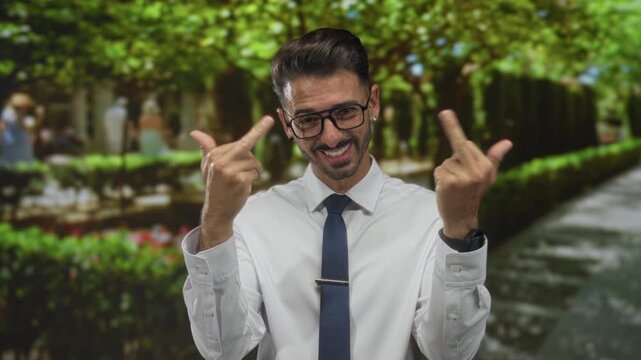 Man in white shirt and blue tie flips middle finger gesture on a forest path lined with green hedges; bold defiance.