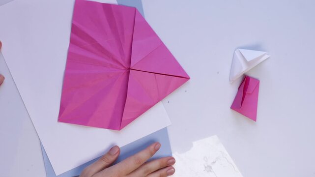 Hands folding pink origami paper in fast motion timelapse craft tutorial