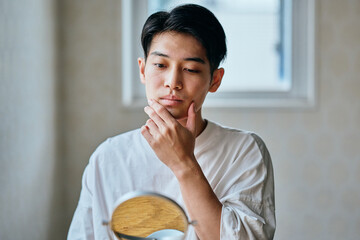 Asian young man checking his skin in mirror at home