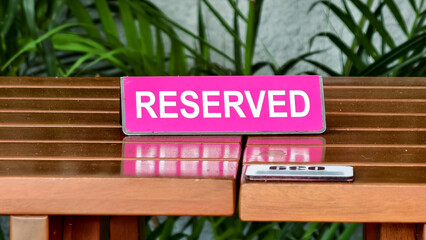 Obraz premium A vivid pink 'RESERVED' sign rests on a polished wooden bench, a gleaming harmonica nearby, suggesting a private spot for quiet reflection or an intimate musical interlude