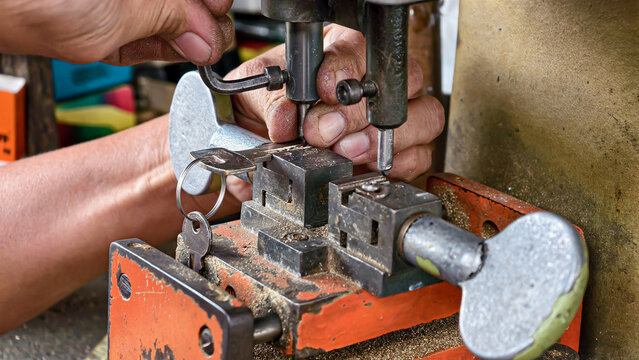Close-up of a skilled craftsman meticulously duplicating a metallic key using a traditional key cutting machine, highlighting precision and manual expertise in locksmithing