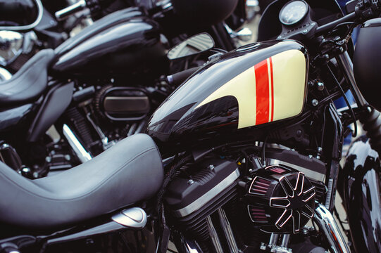 A close-up horizontal shot of a black motorcycle gas tank featuring a stylish cream and red striped graphic. The image captures the sleek design and high-quality paint job of a modern cruiser motorcyc