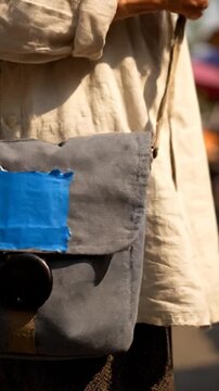 Wrinkled hands resting on a grey fabric bag with blue patch