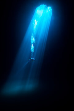 View of diver suspended in the deep blue, illuminated by a single beam of light penetrating the dark abyss in Tulum, Quintana Roo, Mexico.
