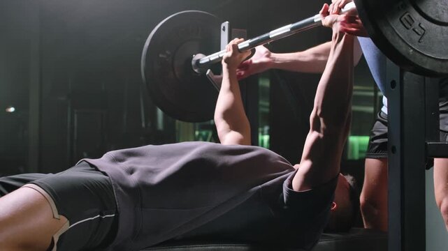 Man doing bench press at gym with spotter providing assistance. Strength training workout scene for fitness and healthy lifestyle.