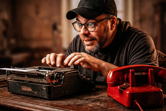 Excited Man Typing Frantically on a Vintage Typewriter Next to a Red Rotary Phone