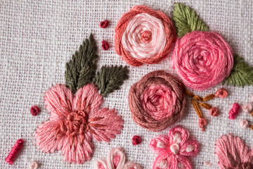 Close-up of pink floral hand embroidery stitched with cotton threads on natural linen fabric. Decorative needlework texture with shallow depth of field and soft pastel tones, handmade craft background