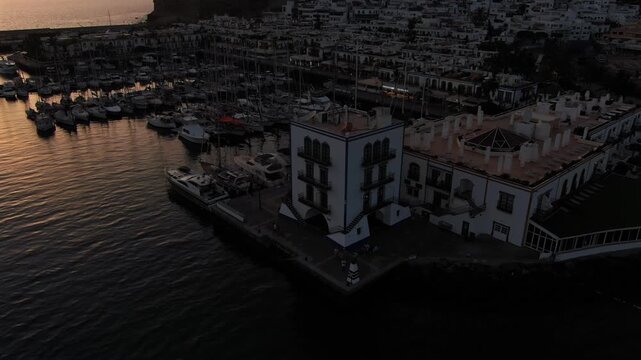 Beautiful aerial perspective of the port of Puerto de Mogan in Gran Canaria during a colorful sunset. The ocean water reflects the warm light