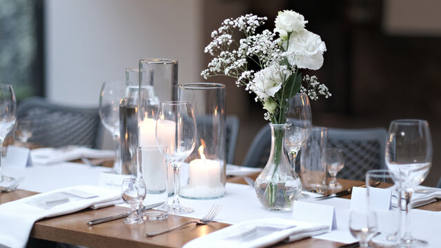 Elegant wedding table setting with white flowers in a vase and burning candles in glass jars