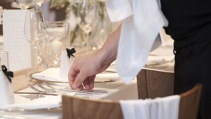 Close-up of a waiter's hand precisely arranging silver forks on a luxurious wedding banquet table
