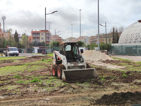 Rome, Italy - February 19, 2026: Bobcat skid steer loader on a construction site with dirt and grass, residential buildings visible in the background