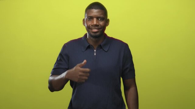 Man smiling giving thumbs up with visible hand and pointing gesture in studio with green backdrop; approval confidence.
