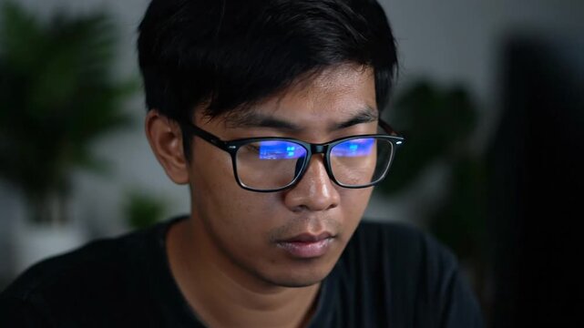 Dedicated young person focusing intensely on a digital screen, blue light reflecting on eyewear, highlighting deep concentration and potential visual strain from prolonged computer use