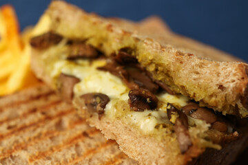 A close-up image of a cheese and sausage toast. Potatoes are also visible in the background.
