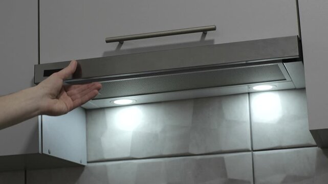 Man pull out a stove extractor hood to turn on ventilation and lights on kitchen. Close up.