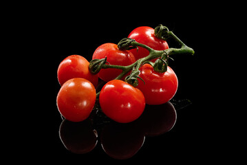 Cherry tomatoes on vine reflecting on black surface