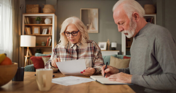 Two seniors examine documents related to life insurance at a table in their living room. They look focused and engaged in their discussion about financial planning.