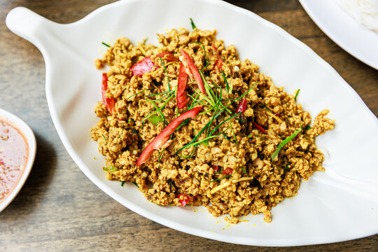 Top view of Kua Kling, Thai dry spicy minced pork curry with herbs and chili, served in a white leaf-shaped plate with shrimp paste sauce.