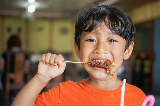 Close up portrait of a young boy enjoying and biting a lamb satay skewer, capturing authentic real food moment and everyday lifestyle