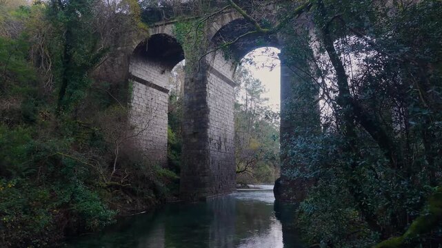 San Crimenzo River With Arches Of Ponte Peon - Stone Viaduct Bridge In Dumbria, Spain. pullback drone shot