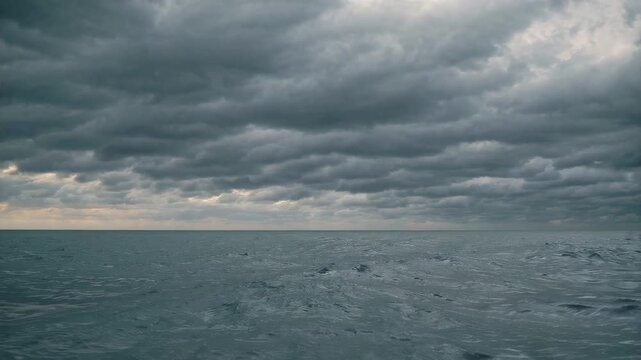 A wide shot of a restless grey ocean under a heavy, overcast sky filled with dark rain clouds. This atmospheric scene captures the power of nature and a somber, cinematic mood.